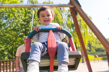 Baby boy in a swing laughing next to his parents