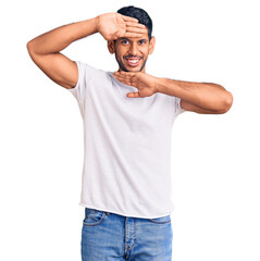 Fototapeta premium Young latin man wearing casual clothes smiling cheerful playing peek a boo with hands showing face. surprised and exited