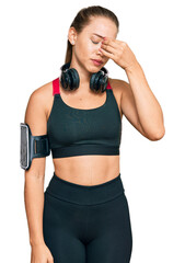 Beautiful blonde woman wearing gym clothes and using headphones tired rubbing nose and eyes feeling fatigue and headache. stress and frustration concept.
