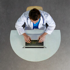 Overhead shot of a doctor sitting on a table looking at a laptop with minimalist background