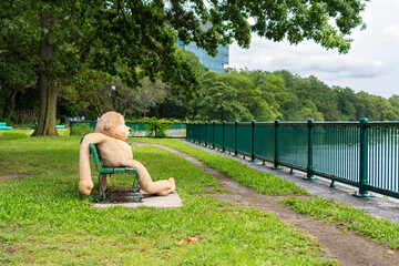 A giant monkey doll relaxing on a bench in front of the Charles River, Watertown, USA