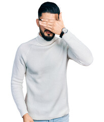 Fototapeta premium Young arab man with beard wearing elegant turtleneck sweater and glasses covering eyes with hand, looking serious and sad. sightless, hiding and rejection concept