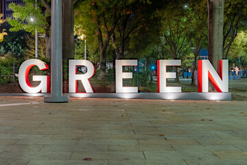 Red and gray three-dimensional 3d letters forming the word GREEN with an evening outdoor...