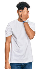 Young arab man wearing casual white t shirt covering one eye with hand, confident smile on face and surprise emotion.