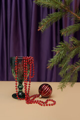 wine glass with dangling red beads and decoration with a Christmas tree branch against the background of curtains. New Year dinner, drink, wine concept