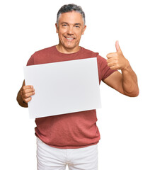 Handsome middle age man holding blank empty banner smiling happy and positive, thumb up doing...