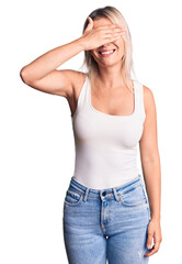 Young beautiful blonde woman wearing casual sleeveless t-shirt smiling and laughing with hand on face covering eyes for surprise. blind concept.