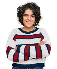 Young hispanic woman with curly hair wearing casual clothes happy face smiling with crossed arms...