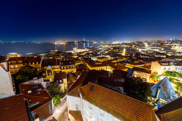 A colorful night sky over the illuminated cityscape, Tagus River, and Ponte 25 de Abril bridge seen...