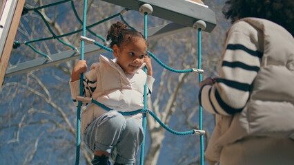African kid climbing rope ladder sunny day. Little girl playing on playground