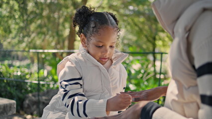 African american girl playing with mom hands sitting bench green park close up.