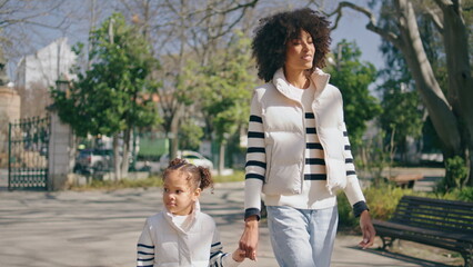 African woman walking girl at sunny park. Mother strolling with lovely daughter.