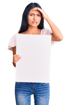 Young beautiful latin girl holding blank empty banner stressed and frustrated with hand on head, surprised and angry face