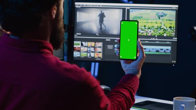 Video editor following tutorial on green screen smartphone, learning to select key frames to use in movie montage. Freelancing applying editing techniques seen online on chroma key phone