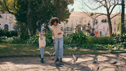 African child feeding birds with mother in park. Girl throwing food to pigeons.