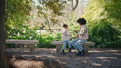 Mother clapping hands daughter sitting bench green park. African mom play girl 