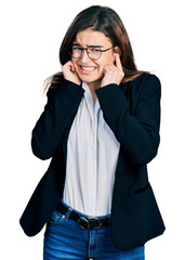 Young caucasian girl wearing business style and glasses covering ears with fingers with annoyed expression for the noise of loud music. deaf concept.