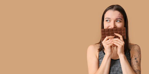 Sporty young woman holding chocolate bar on beige background with space for text