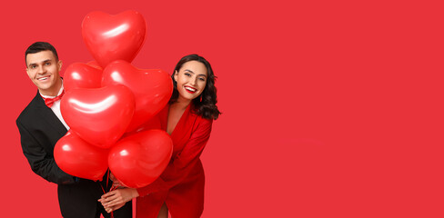 Loving young couple with heart-shaped balloons on red background with space for text. Valentine's Day celebration