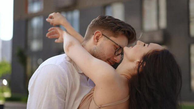 Slow motion. Close-up. A beautiful couple theatrically embraces against the backdrop of a modern building. A man gently kisses a woman on the neck