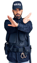 Young hispanic man wearing police uniform rejection expression crossing arms doing negative sign, angry face