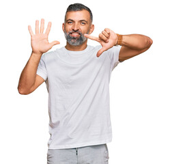 Middle age handsome man wearing casual white tshirt showing and pointing up with fingers number seven while smiling confident and happy.