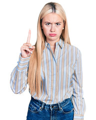 Beautiful blonde woman pointing up with finger skeptic and nervous, frowning upset because of...