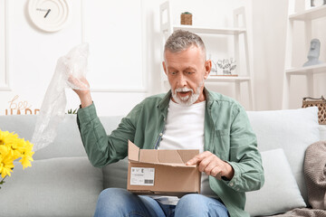 Surprised mature man unpacking parcel at home