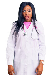 Young african american woman wearing doctor stethoscope in shock face, looking skeptical and...