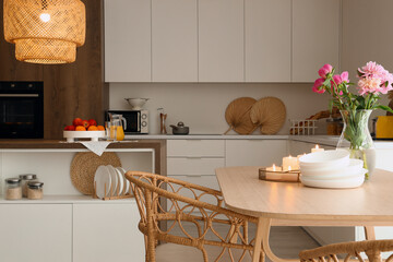 Dining table with peony flowers, burning candles and bowls in modern kitchen with glowing lamp