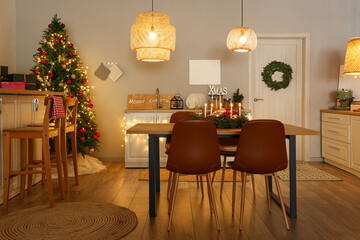 Interior of modern kitchen with glowing lamps, dining table and Christmas tree at evening