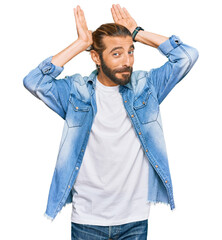 Attractive man with long hair and beard wearing casual denim jacket doing bunny ears gesture with...