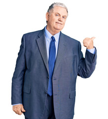 Senior grey-haired man wearing business jacket smiling with happy face looking and pointing to the side with thumb up.