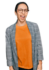 Young hispanic girl wearing business jacket and glasses winking looking at the camera with sexy...