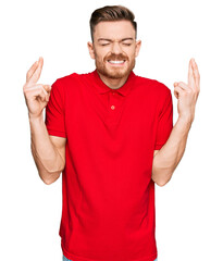 Young redhead man wearing casual clothes gesturing finger crossed smiling with hope and eyes closed. luck and superstitious concept.