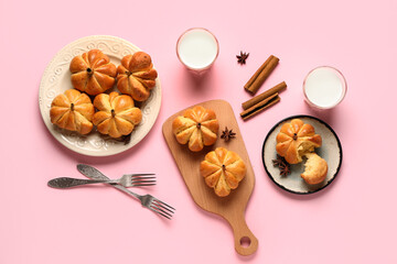 Tasty pumpkin shaped buns and glasses of milk on pink background