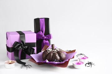 Delicious chocolate cake, gift boxes, burning candles and spiders for Halloween celebration on white background