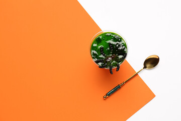 Plastic cup with delicious panna cotta and spoon for Halloween celebration on color background