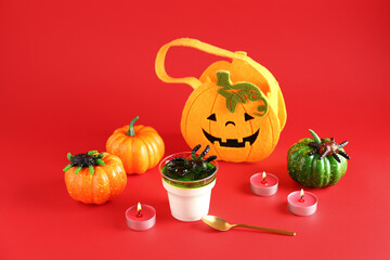 Plastic cup with delicious panna cotta, burning candles and pumpkins for Halloween celebration on red background