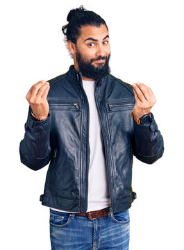 Young arab man wearing casual leather jacket doing money gesture with hands, asking for salary payment, millionaire business