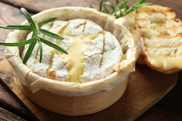 Tasty baked brie cheese, bread and rosemary on wooden board, closeup