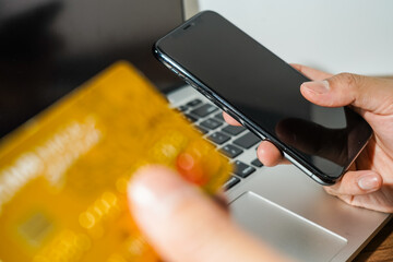 Close up male hand holding a bank credit card doing online transactions using a laptop and smart phone