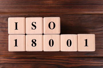 Cubes with abbreviation ISO and number 18001 on wooden table, flat lay