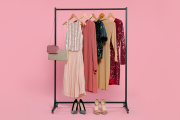 Rack with stylish women's clothes on wooden hangers, accessories and shoes against pink background