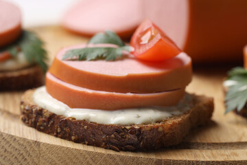 Delicious sandwich with boiled sausage, tomato and sauce on board, closeup