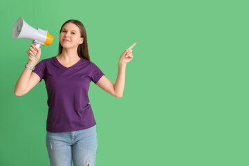 Young woman with megaphone pointing at something on green background