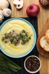 Bowl of tasty cream soup with mushrooms, green onions and dill on wooden table, flat lay