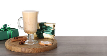 Delicious eggnog in glass, spices and gift boxes on wooden table against white background, space for text