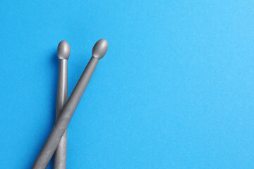 Two gray drum sticks on light blue background, top view. Space for text