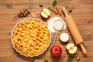 Baking dish with delicious apple pie and ingredients on wooden background